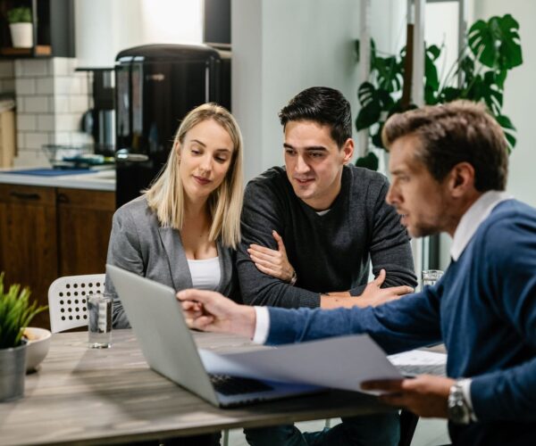 young-couple-real-estate-agent-using-laptop-while-going-through-housing-plan-meeting-min-600x5001.jpg